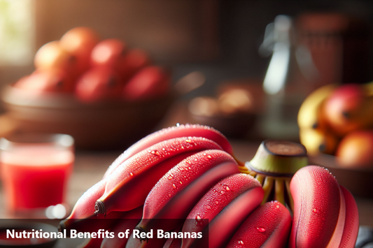 A close-up image of a bunch of red bananas with water droplets on their skin, sitting on a wooden table with a blurred background of other fruits and a glass of red banana juice.